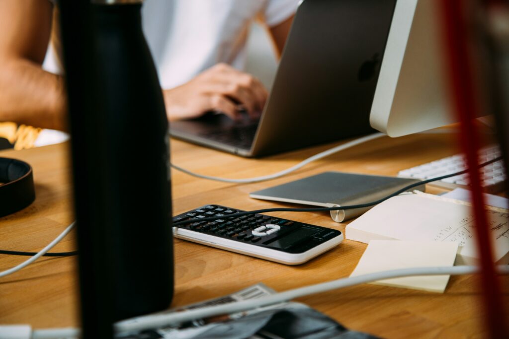 Table de travail avec un ordinateur portable, une calculatrice et des notes manuscrites, illustrant la gestion comptable pour les freelances avec Neovi.