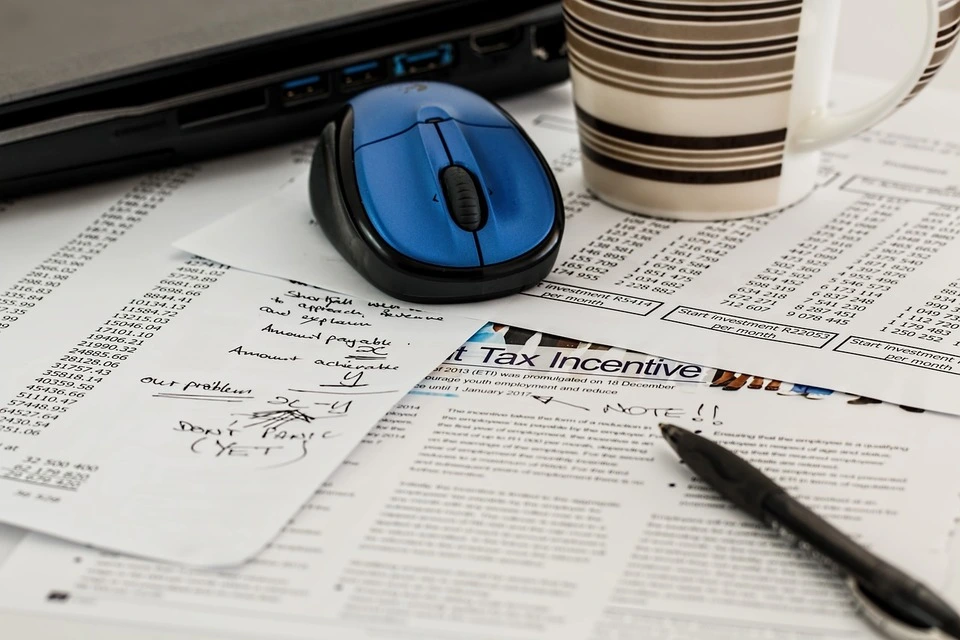 Documents administratifs, souris d'ordinateur et tasse de café sur un bureau, symbolisant les démarches pour passer d'une auto-entreprise à une société.