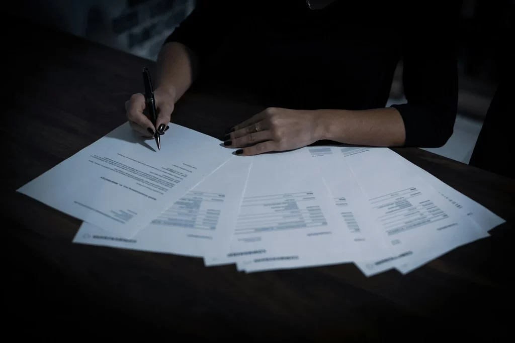 Main signant un document officiel, entourée de feuilles administratives, illustrant la déclaration ou l’utilisation de chèques CESU pour les freelances.