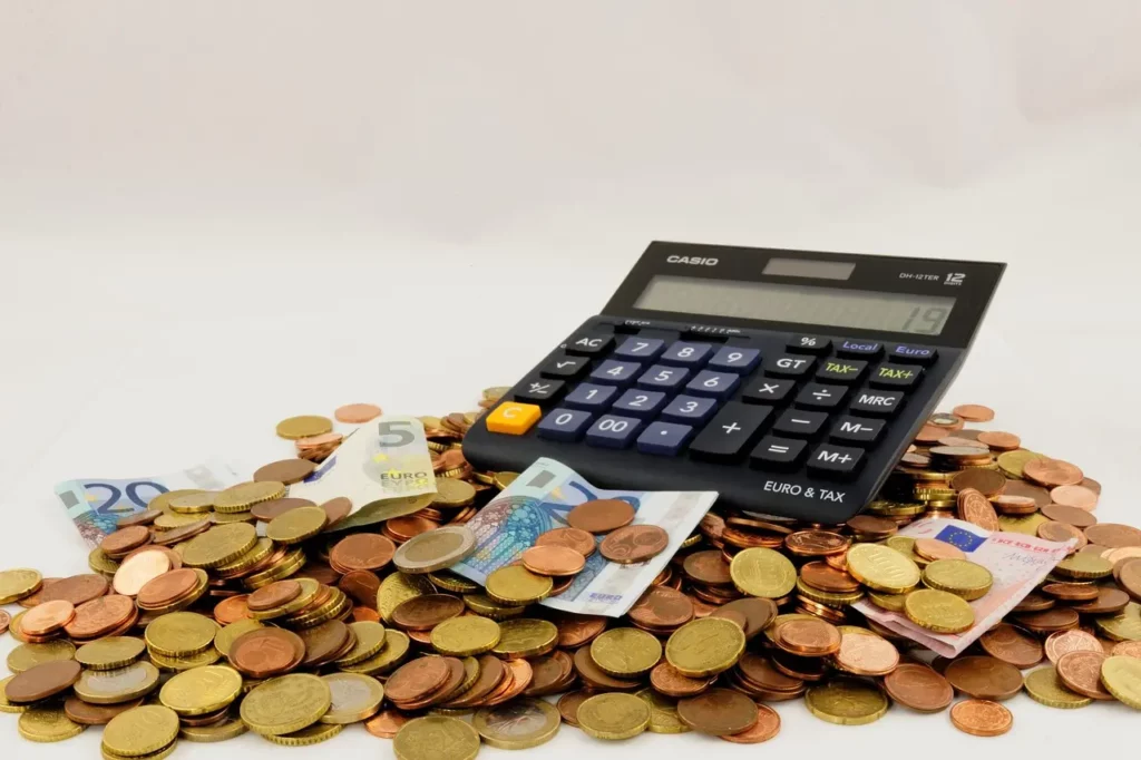 Calculatrice posée sur un tas de pièces et de billets en euros, illustrant le calcul de la taxe PUMA pour les freelances.