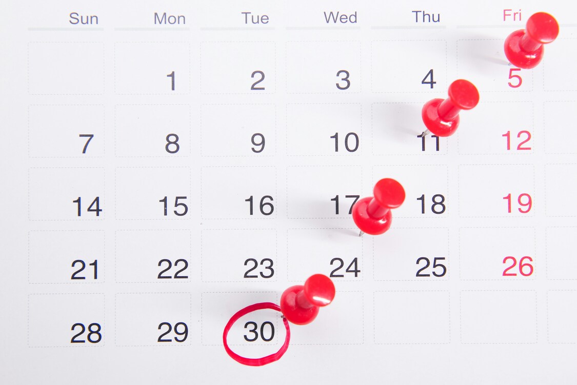 Calendrier avec des punaises rouges et une date encerclée, symbolisant les échéances fiscales importantes des freelances en 2025.