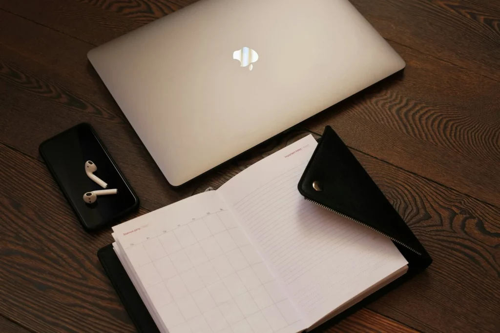 Matériel de freelance : ordinateur portable, agenda et écouteurs sur un bureau en bois.