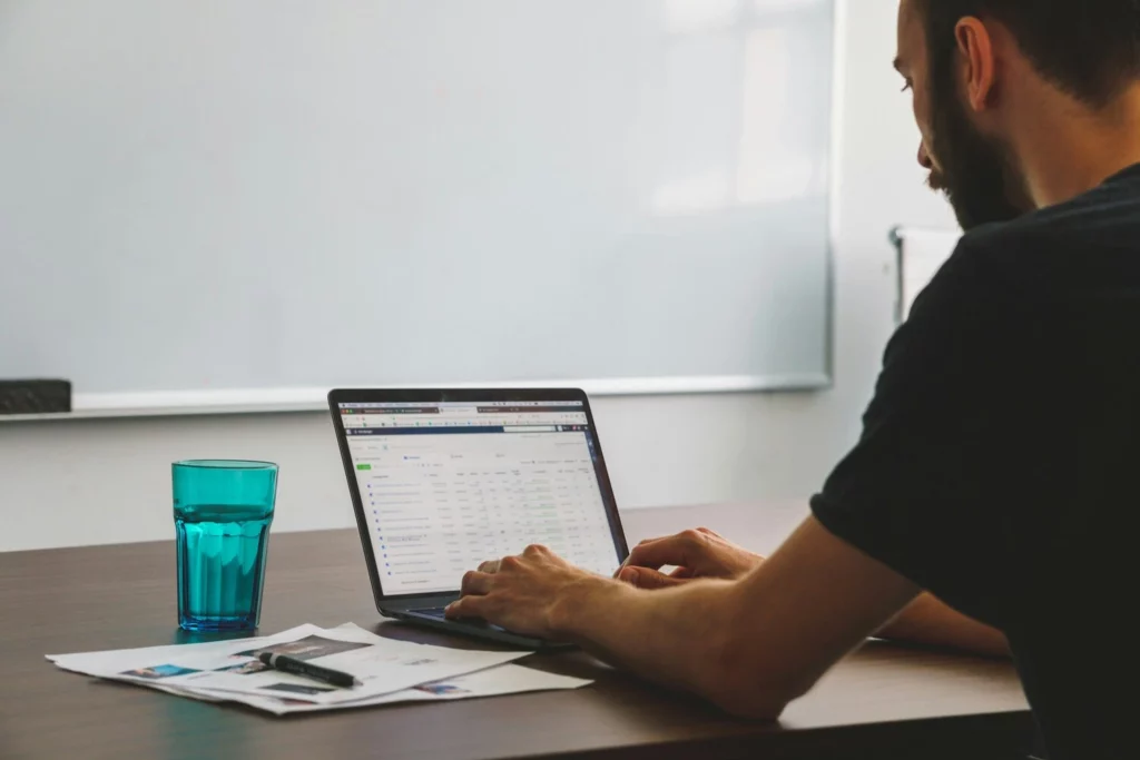 Freelance consultant travaillant sur un ordinateur portable avec des documents et un verre d’eau sur la table.