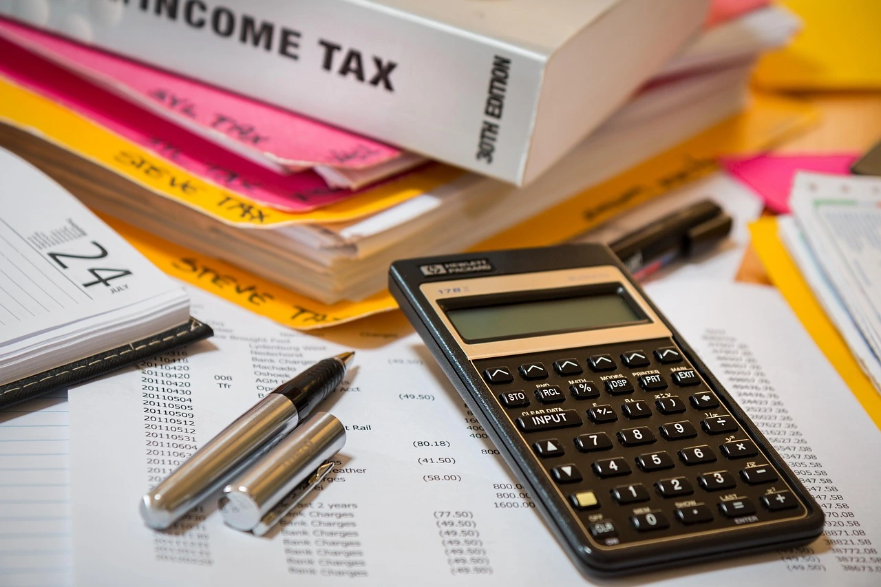 Calculatrice posée sur des documents fiscaux avec dossiers et stylos.