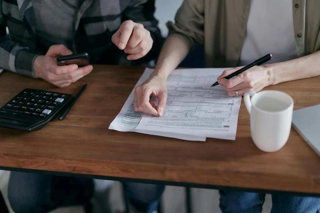 Deux personnes remplissant un formulaire administratif avec une calculatrice à côté.