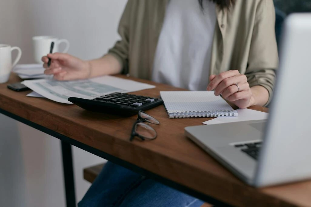 Auto-entrepreneur travaillant sur ses factures avec une calculatrice et un ordinateur portable.