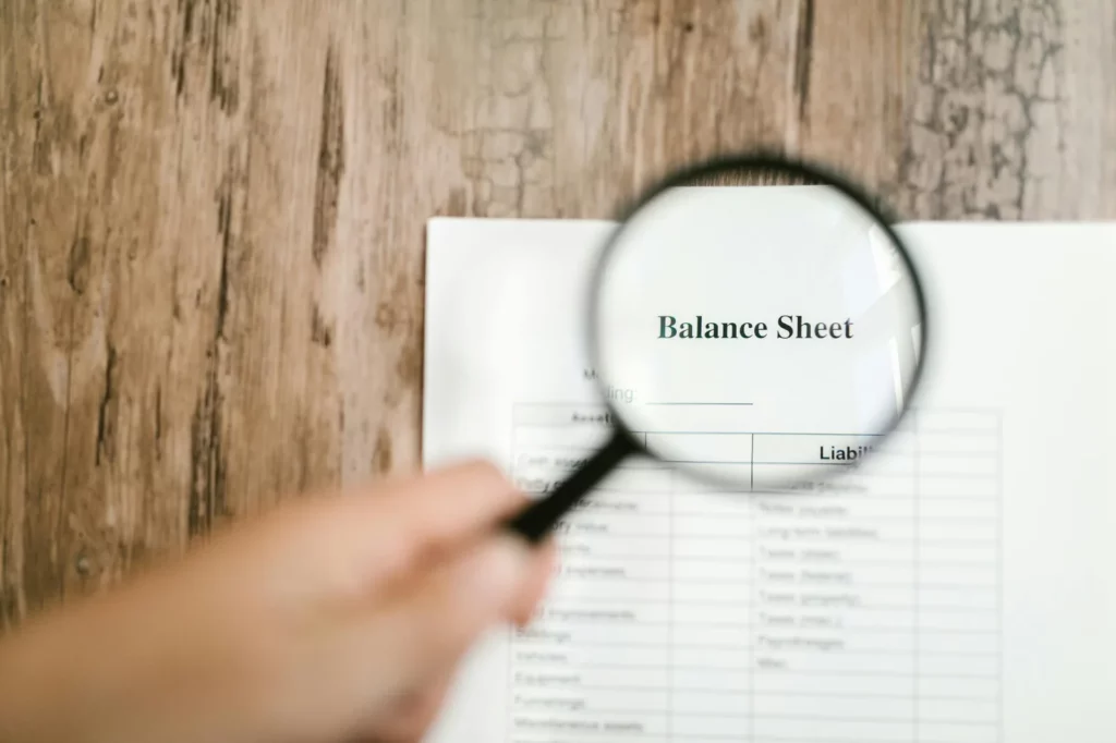 Loupe pointée sur un document intitulé "Balance Sheet" posé sur une table en bois.