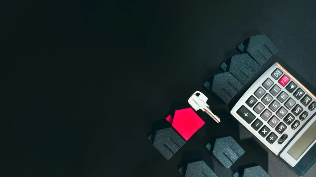 Clé posée sur une maison miniature rouge avec calculatrice